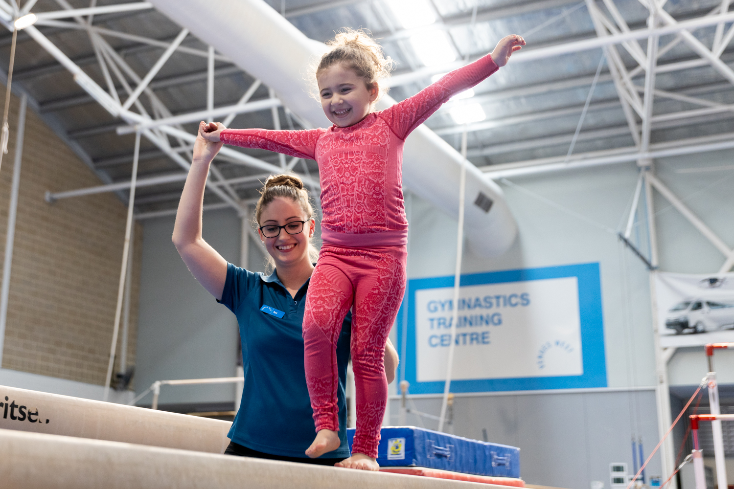 Gymnastics coach assisting a young girl walk on the balance beam
